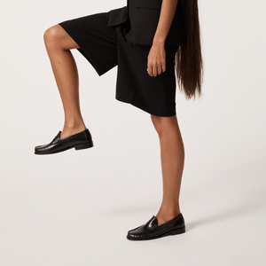 Woman holding leg up wearing black penny loafers