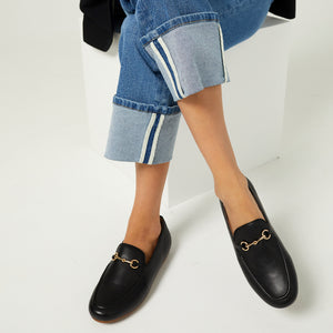  Model with crossed legs showcasing a pair of Linden Loafer shoes in Black, highlighting their elegant design and comfortable fit
