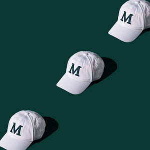  3 white Millwoods caps at 3/4 front view against a dark green background, providing a stylish contrast and highlighting the white hats for your active wardrobe