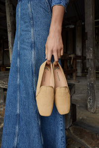 In a close-up image from the Autumn/Winter 2024 campaign, a model holds up a pair of champagne Aspen slippers, showcasing intricate details in a double presentation.