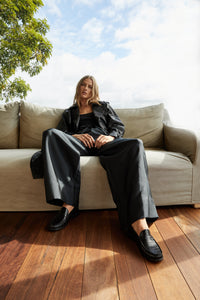 Model in black sitting on a couch, showcasing Penny Loafer in Black Croc, highlighting the stylish and comfortable design of the shoes