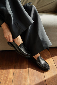 Close-up of shoes: model showcasing Penny Loafer in Black Croc, emphasizing the elegant details and stylish embossed crocodile pattern of the shoes.