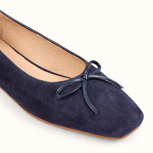 Navy blue suede ballerina shoe with a bow on a white background