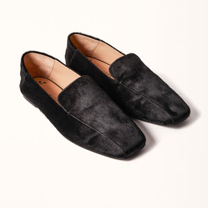 A pair of black ballet flats with a square toe design made of pony hair material, displayed in a 3/4 view.