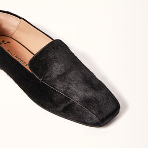 A single black ballet flat with a square toe design crafted from pony hair material, shown in a 3/4 view