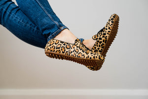 Close-up of a model's legs crossing over, showcasing Linden Loafer shoes in Leopard print, highlighting their elegant design and comfortable fit.